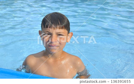 Cute little boy in the swimming pool on summer day. Summer and happy childhood concept. Copy space in bright blue water. Cute little boy in the swimming pool on summer day. Summer and happy childhood concept. Copy space in bright blue water. 136391655