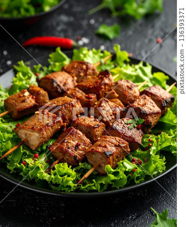Roasted goat meat skewers seasoned with local spices rest on bed of fresh leafy green vegetables. 136393371