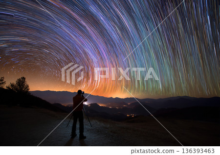 An astronomer is taking a long-exposure photograph of a starry sky, capturing beautiful light trails and celestial movement 136393463