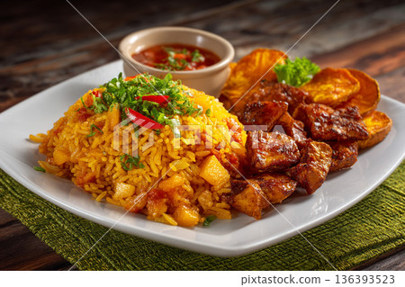 A plate of freshly cooked Guinean Jollof rice served with fried sweet potatoes and spicy tomato sauce. 136393523