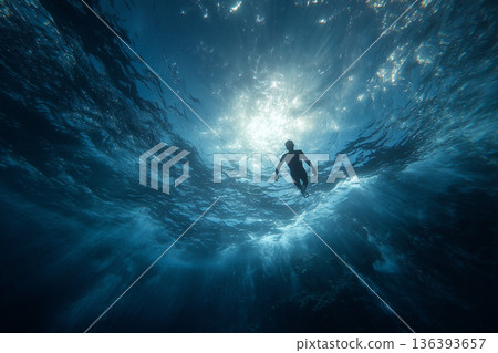 A freediver's perspective: looking up at the shimmering surface, seeing a distant boat and streaks of sunlight far above. 136393657