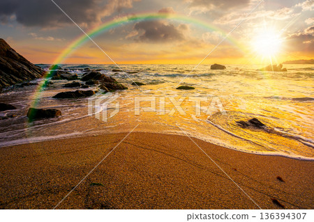 beautiful sunset over empty sandy beach at the sea. white foam rolling on to the shore near boulder in evening light with rainbow. perfect summer vacation concept. awesome weekend. low angle view 136394307