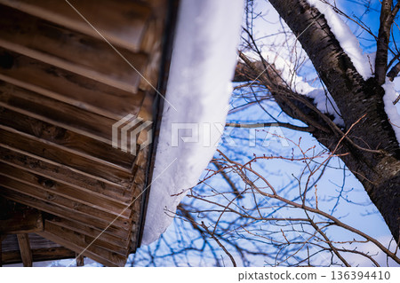 晴天下雪的危險:積雪從屋頂滑落,藍天白雲。 晴天下雪的危險:積雪從屋頂滑落,藍天白雲。 136394410