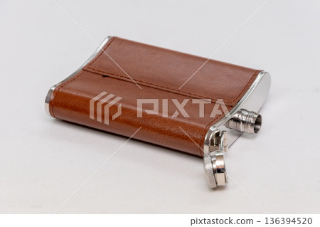 Metal flask in leather cover lies on a light background. 136394520