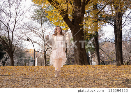 秋日公園裡,年輕女子站在落滿銀杏葉的公園裡。 秋日公園裡,年輕女子站在落滿銀杏葉的公園裡。 136394533