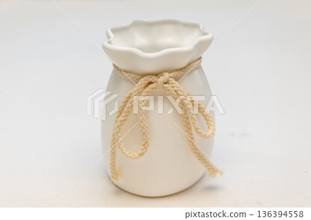 White ceramic vase tied with decorative rope on a light background. 136394558