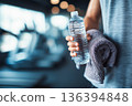 Close up of faceless man holding towel and water bottle in gym with copy space. Post workout wellness recovery, hydration, healthy lifestyle, motivation, daily fitness, wellness discipline. 136394848