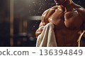 Strong muscular faceless man standing in dim gym environment with sweat droplets, wiping down after an intense workout. Fitness, copy space, strength training program, bodybuilding, athletic. 136394849