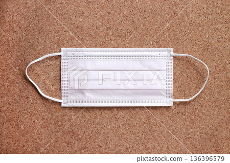 A four-ply pleated nonwoven mask laid flat on a cork background. A daily hygiene material. 136396579