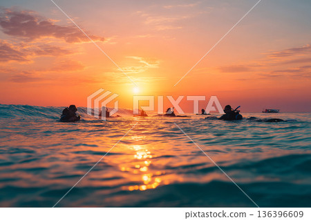 The serene scene of multiple snorkelers gently drifting across calm, shallow water at sunset, their forms silhouetted softly. The serene scene of multiple snorkelers gently drifting across calm, shallow water at sunset, their forms silhouetted softly. 136396609