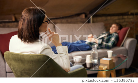 Teenage boy lying on couch during psychotherapy session with psychologist. Teenage boy lying on couch during psychotherapy session with psychologist. 136396782