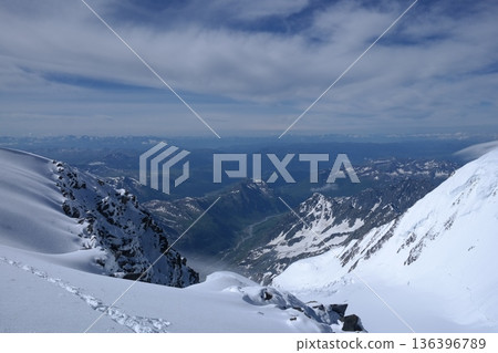 A stunning rock formation covered in snow, set against a clear blue sky with fluffy clouds in the background, creating a peaceful and breathtaking mountain landscape. 136396789