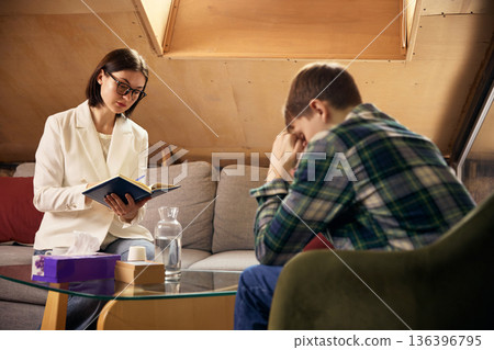 Teenage boy emotional during psychology therapy while specialist takes notes. Teenage boy emotional during psychology therapy while specialist takes notes. 136396795