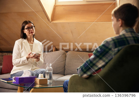 Teenage boy talking with female psychologist during therapy session. 136396796