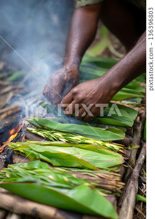 A close-up of "Lovo" (earth oven) cooking in progress, with smoky steam rising from banana leaves, highlighting traditional methods. 136396803