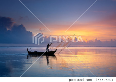A local fisherman casting his net into the calm, emerald waters of a lagoon at sunrise, a timeless act of sustenance. A local fisherman casting his net into the calm, emerald waters of a lagoon at sunrise, a timeless act of sustenance. 136396804