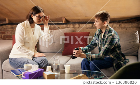 Teenage boy showing smartphone to female psychologist during therapy session Teenage boy showing smartphone to female psychologist during therapy session 136396820