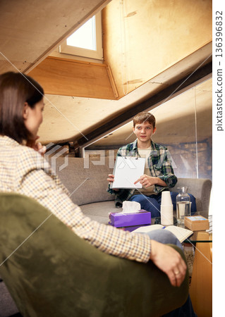 Teenage boy showing clipboard to female psychologist. Teenage boy showing clipboard to female psychologist. 136396832