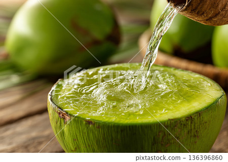 A close-up of Comorian coconut water being freshly poured from a green coconut, emphasizing natural refreshment and tropical bounty. A close-up of Comorian coconut water being freshly poured from a green coconut, emphasizing natural refreshment and tropical bounty. 136396860