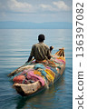 A Malawian fisherman paddling a traditional wooden canoe on Lake Malawi with colorful nets and calm waters. 136397082