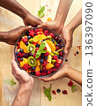 A diverse group of hands prepares a colorful healthy fruit salad, promoting diabetes-friendly eating. 136397090