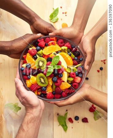 A diverse group of hands prepares a colorful healthy fruit salad, promoting diabetes-friendly eating. 136397090