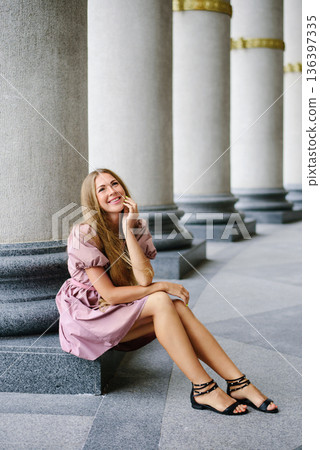 Relaxed Woman In Pink Dress Sitting By Columns 136397335