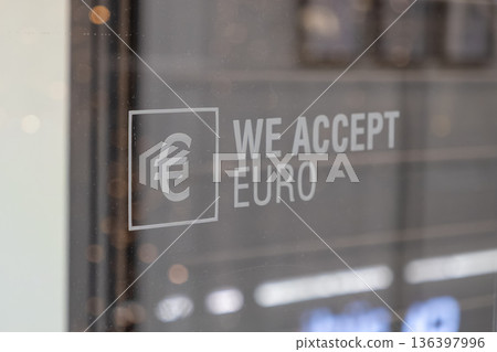Euro currency symbol and text WE ACCEPT EURO displayed on a shop window, representing payment methods and facilitating international business operations 136397996
