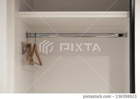 Clean empty white wardrobe interior with modern wooden hangers on a shining chrome rod and top shelf, representing home organization and storage solutions 136398023