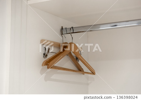 Three empty wooden hangers hang neatly on a shiny chrome rod inside a minimalist white closet, symbolizing clean clothing organization and home storage solutions 136398024
