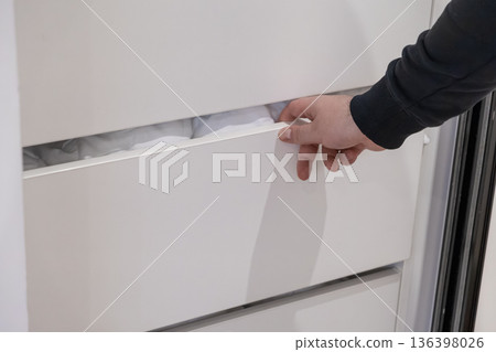 Man's hand reaching to open a white minimalist drawer filled with clean white linens, highlighting efficient home organization and storage solutions for a tidy space 136398026
