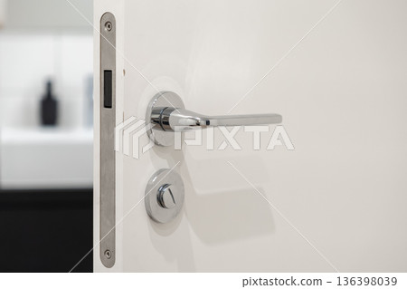 Modern chrome door handle and secure lock on a clean white door, slightly ajar, symbolizing privacy, home access, and contemporary interior design Modern chrome door handle and secure lock on a clean white door, slightly ajar, symbolizing privacy, home access, and contemporary interior design 136398039