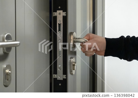 A person's hand gripping a modern metallic door handle on a secure gray entrance door, emphasizing safety and privacy for home or office access A person's hand gripping a modern metallic door handle on a secure gray entrance door, emphasizing safety and privacy for home or office access 136398042