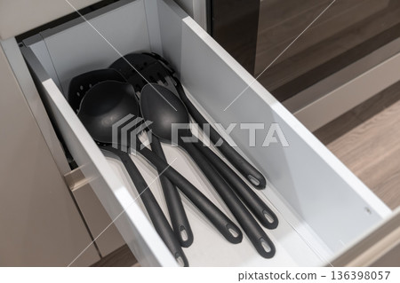 A well-organized modern kitchen drawer filled with various sleek black cooking utensils, ideal for culinary tasks, emphasizing home efficiency and smart storage 136398057