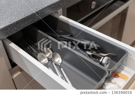Open kitchen drawer neatly organized with various kitchen utensils and cutlery in a modern grey storage tray, representing home organization and efficient cooking space 136398058