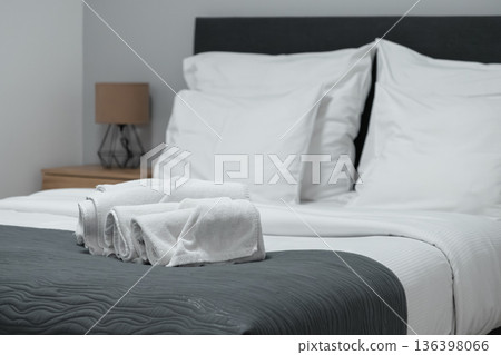 Neatly folded white towels resting on a grey throw blanket on a modern bed in a comfortable hotel room, symbolizing hospitality and comfort Neatly folded white towels resting on a grey throw blanket on a modern bed in a comfortable hotel room, symbolizing hospitality and comfort 136398066