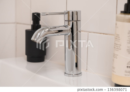 Modern chrome bathroom faucet with sleek design and shiny finish on a pristine white ceramic sink, essential for personal hygiene and home sanitation Modern chrome bathroom faucet with sleek design and shiny finish on a pristine white ceramic sink, essential for personal hygiene and home sanitation 136398071