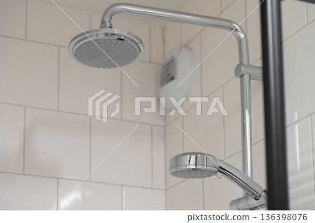 Contemporary chrome shower system with both overhead rain and a flexible handheld head, installed on clean white tiled bathroom walls 136398076