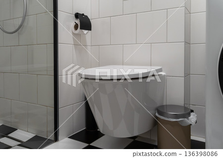 Wall-mounted white ceramic toilet with sleek modern design and a toilet paper holder, emphasizing contemporary bathroom hygiene and minimalist home aesthetics Wall-mounted white ceramic toilet with sleek modern design and a toilet paper holder, emphasizing contemporary bathroom hygiene and minimalist home aesthetics 136398086