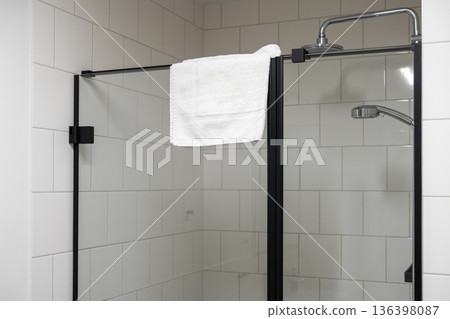 Modern shower cabin with black-framed glass door, featuring a fresh white towel and sleek chrome fixtures, ideal for contemporary bathroom design and hygiene concepts Modern shower cabin with black-framed glass door, featuring a fresh white towel and sleek chrome fixtures, ideal for contemporary bathroom design and hygiene concepts 136398087