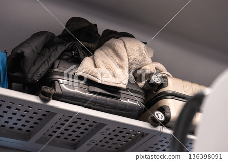 Packed suitcases, warm clothing stacked on overhead luggage rack inside public transport, representing organized long-distance travel Packed suitcases, warm clothing stacked on overhead luggage rack inside public transport, representing organized long-distance travel 136398091