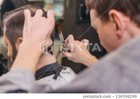 Barber cutting male client hair with scissors and comb. Close up of professional haircut process, precision technique, men grooming service in modern barbershop. 136398299