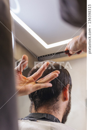 Barber cutting male client hair with scissors and comb. Close up of professional haircut process, precision technique, men grooming service in modern barbershop. 136398315