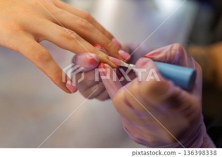 Close up of professional manicure process. Nail technician applying gel polish on female nails with brush while wearing protective gloves in beauty salon Close up of professional manicure process. Nail technician applying gel polish on female nails with brush while wearing protective gloves in beauty salon 136398338
