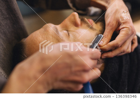 Close up of professional barber shaving male neck with straight razor in barbershop. Beard contouring, classic wet shave, men grooming service and barber work process concept. 136398346
