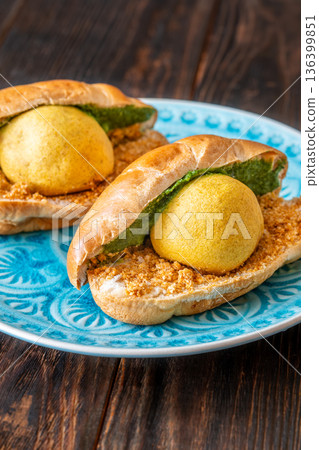 Authentic Vada Pav Indian street food with spicy chutney on rustic wooden background Authentic Vada Pav Indian street food with spicy chutney on rustic wooden background 136399851