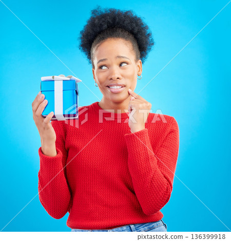 Thinking, winner and black woman with a present, box and celebration against a blue studio background. Female person, doubt or model with a gift, giveaway product or package with surprise and curious Thinking, winner and black woman with a present, box and celebration against a blue studio background. Female person, doubt or model with a gift, giveaway product or package with surprise and curious 136399918