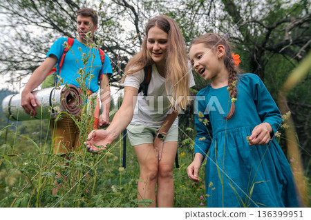 A family enjoys a nature outing, discovering plants and bonding closely in a serene outdoor setting 136399951