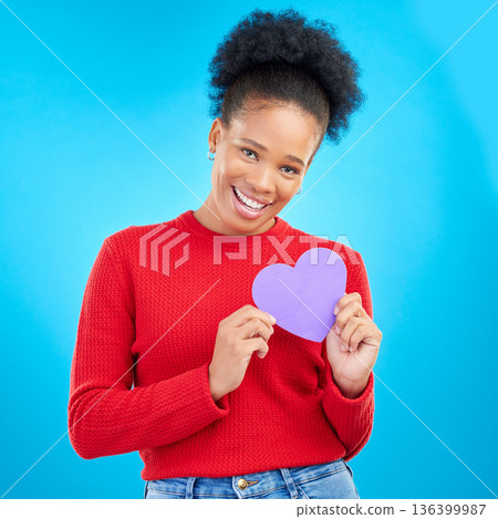 Woman, portrait and heart cut out with a smile for love and valentines day in studio. African female person, blue background and romance emoji icon for kindness with a young happy model and paper 136399987