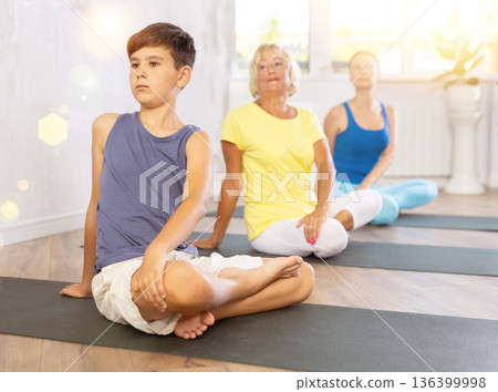 Preteen boy practicing revolved half lotus pose of yoga in light fitness room Preteen boy practicing revolved half lotus pose of yoga in light fitness room 136399998